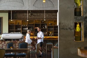 A bar area with a coffee machine, shelves with bottles, and hanging lights.