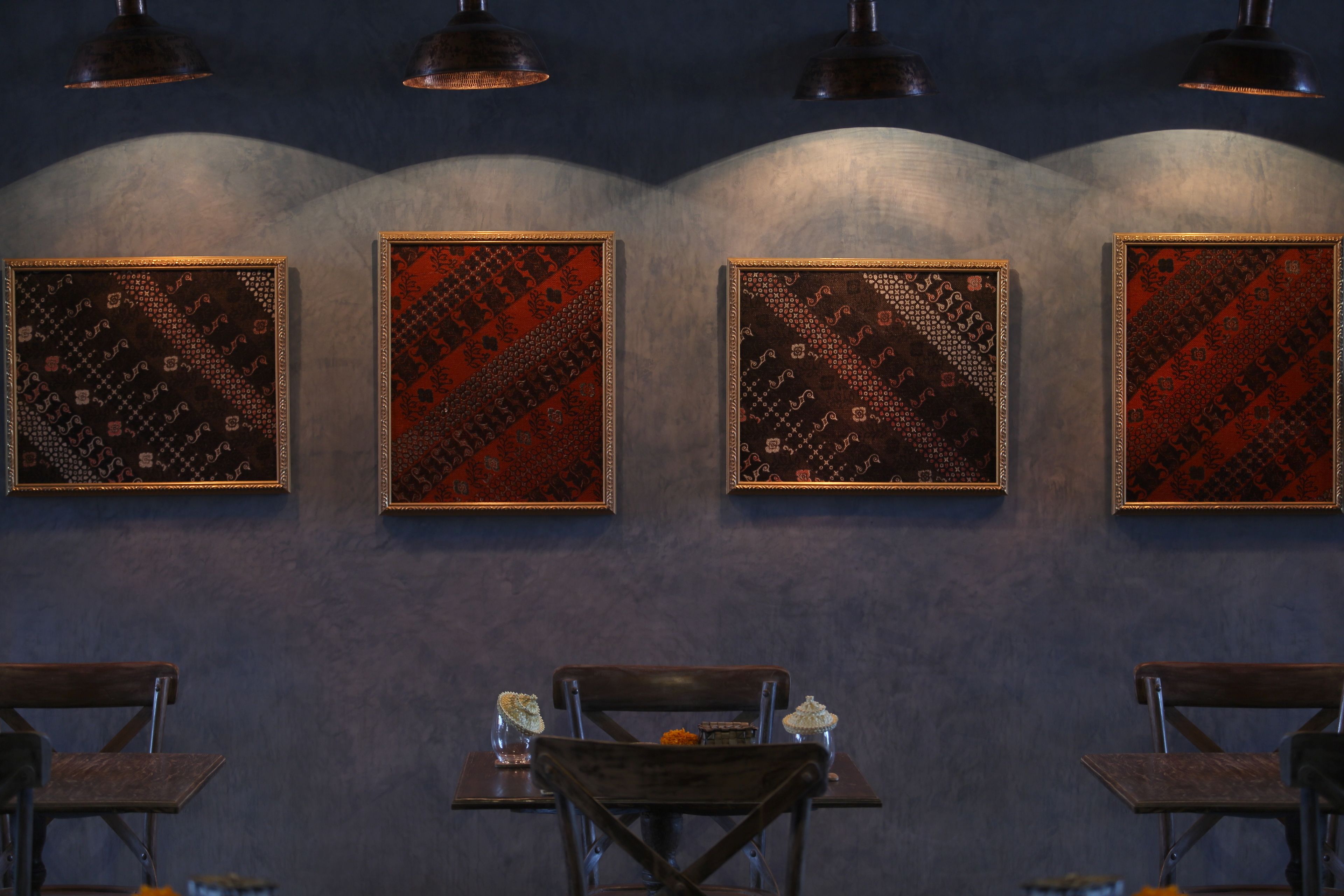A restaurant interior with four framed wall art pieces, wooden tables, and hanging pendant lights.