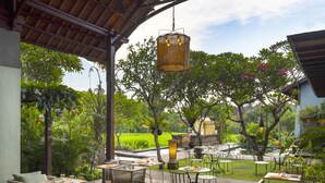 Un patio al aire libre con mesas y sillas, rodeado de abundante vegetación y vistas a un campo de arroz.