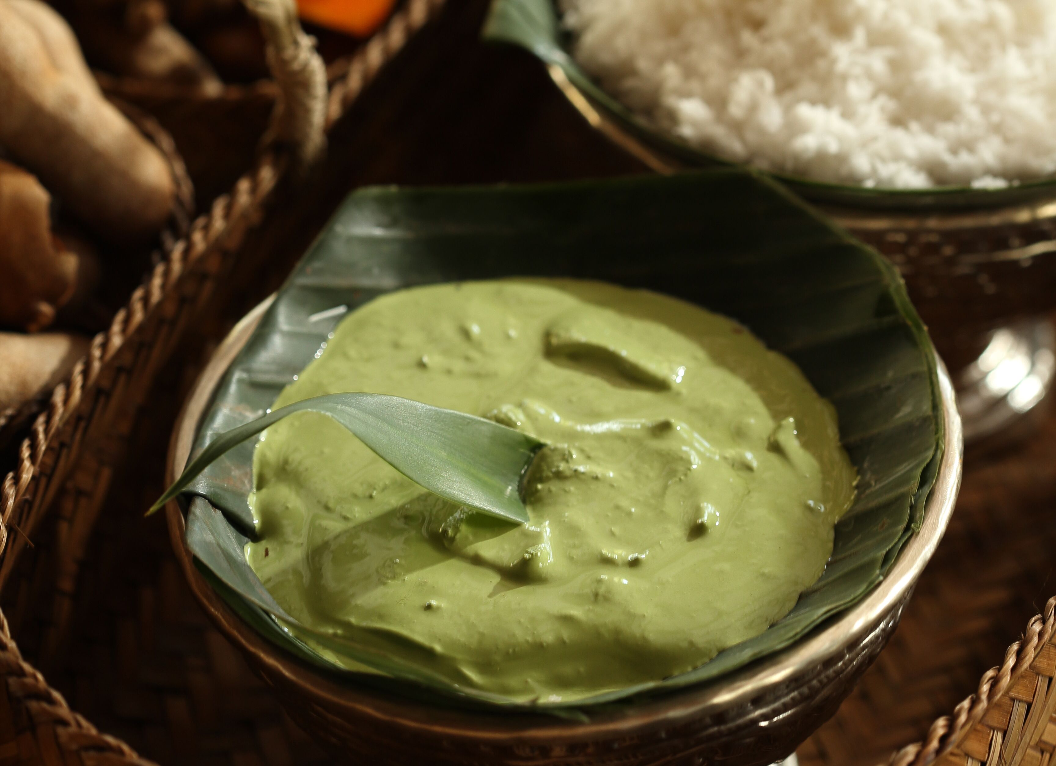 Un tazón de curry verde con una cuchara, sobre un tapete tejido.