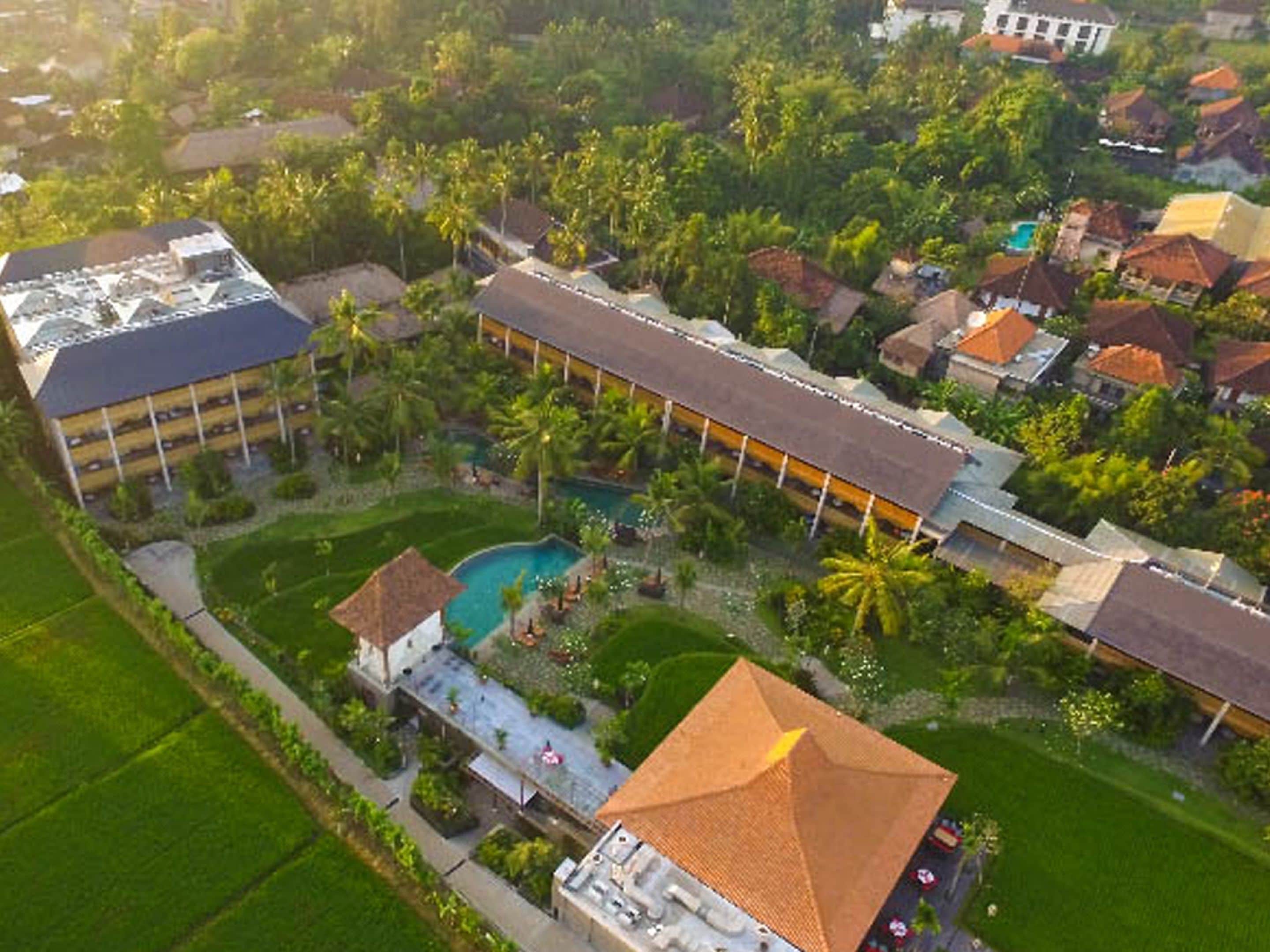 An aerial view of a resort with a swimming pool, multiple buildings, and lush greenery.