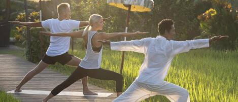 Three people practicing yoga on a wooden deck surrounded by grass.