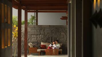 A couple sitting on a sofa in a covered outdoor area with a stone wall featuring carvings.