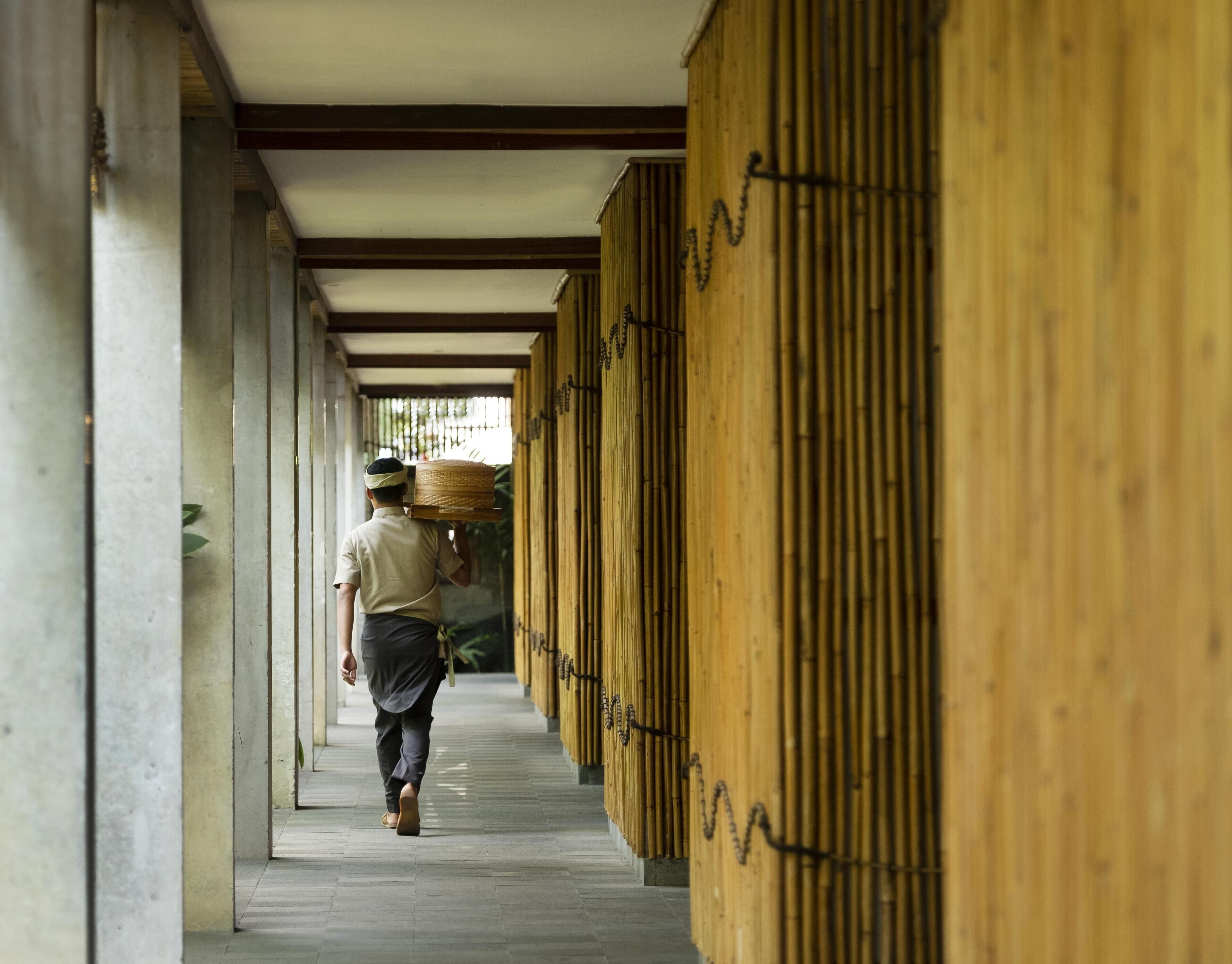 A corridor with bamboo walls and a person carrying a basket.