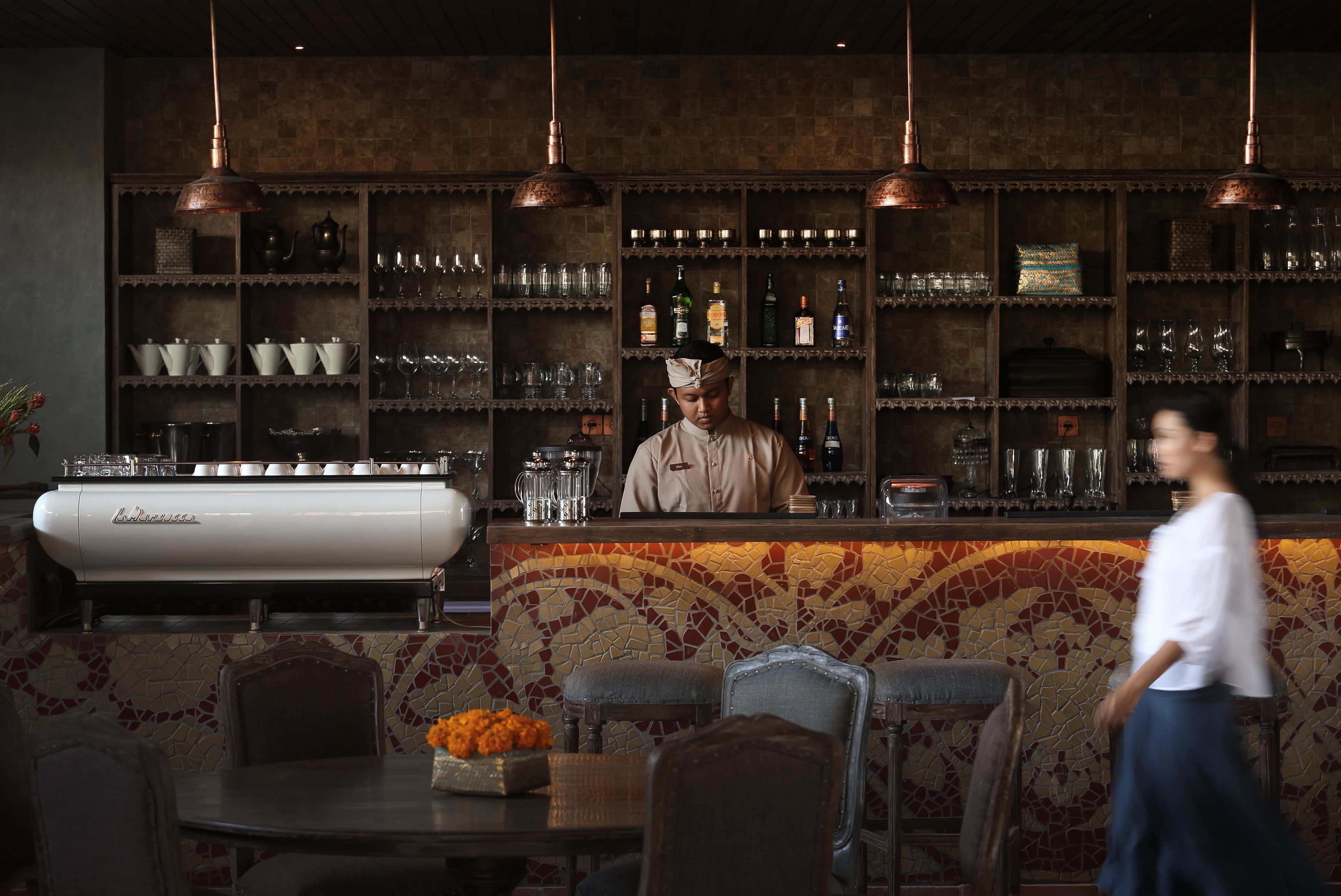 Un espace bar avec un barman, des étagères remplies de verres et de bouteilles, et un comptoir avec une machine à café.