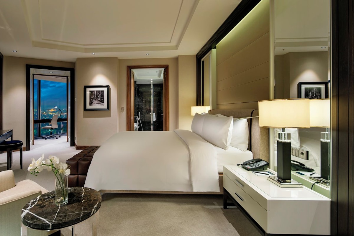 A hotel room with a bed, a desk, a chair, a TV, and a bathroom.