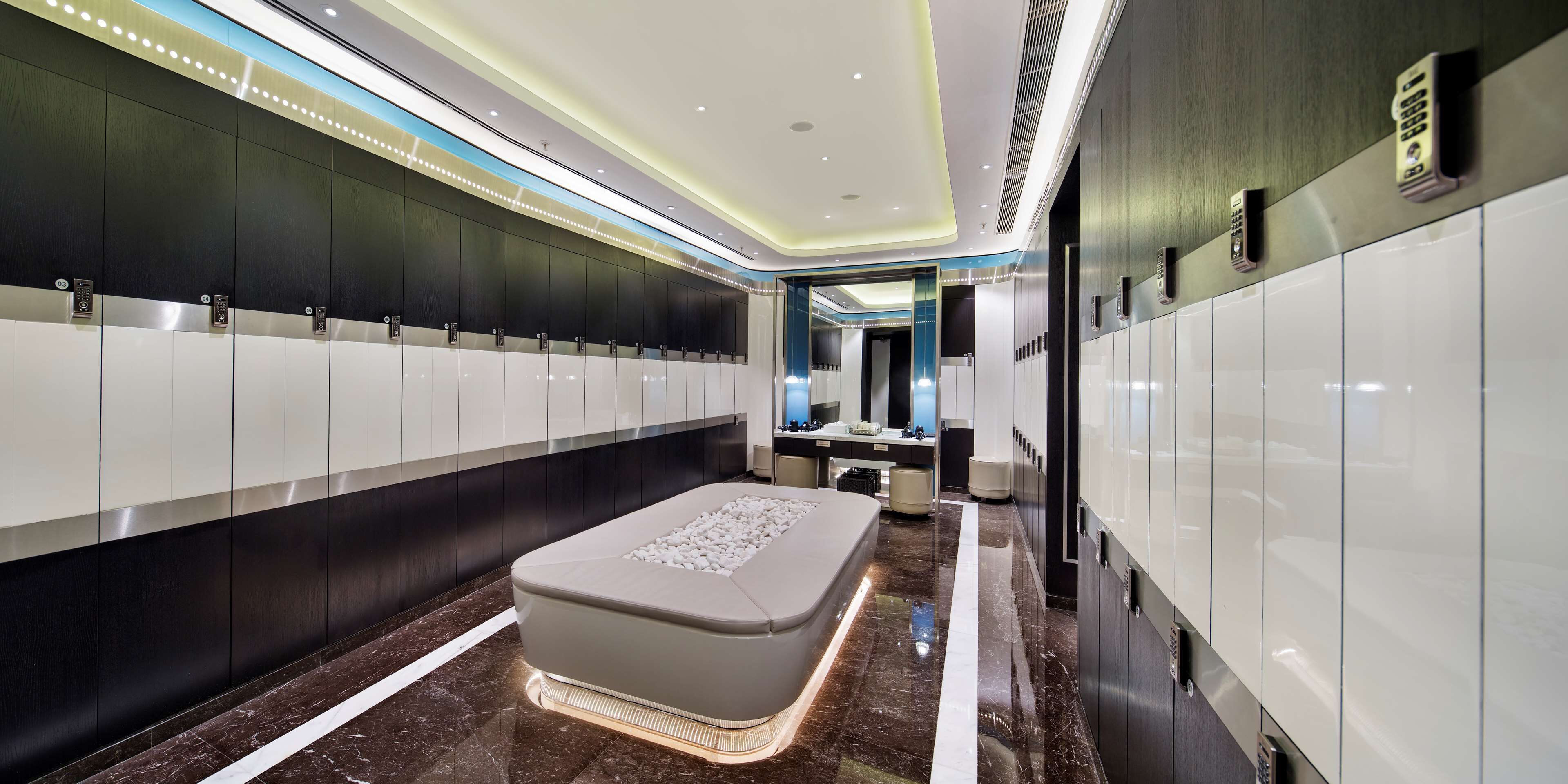 A modern hotel restroom with a long row of lockers, a central bench, and a vanity area.
