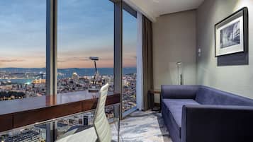 A modern hotel room with a large window offering a city view, a comfortable sofa, and a framed artwork on the wall.