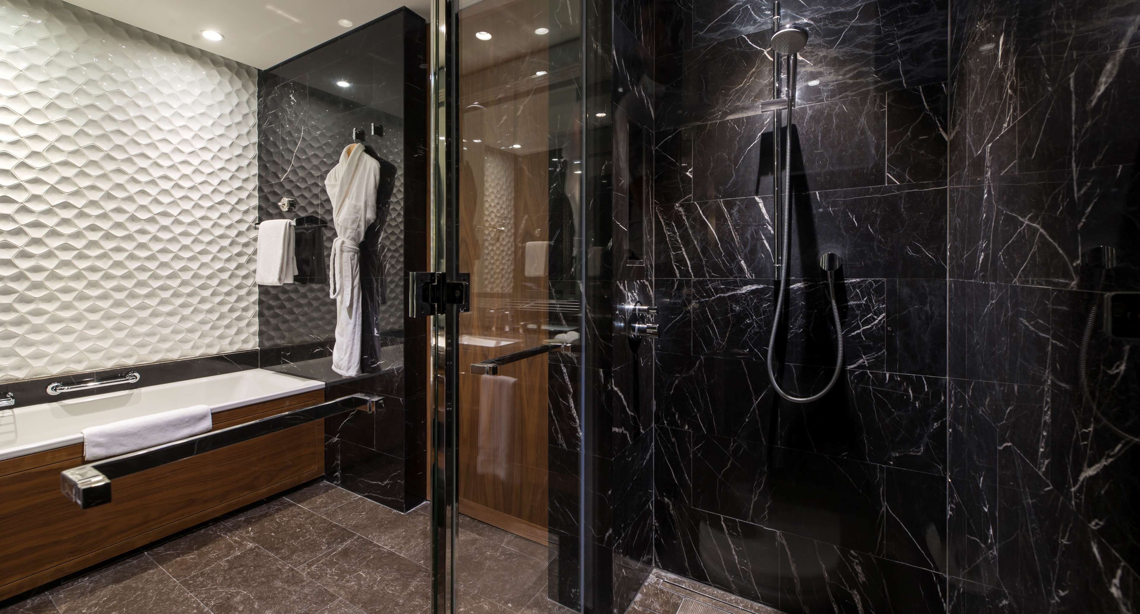 A modern bathroom with a glass-enclosed shower, a wooden vanity, and a textured wall.