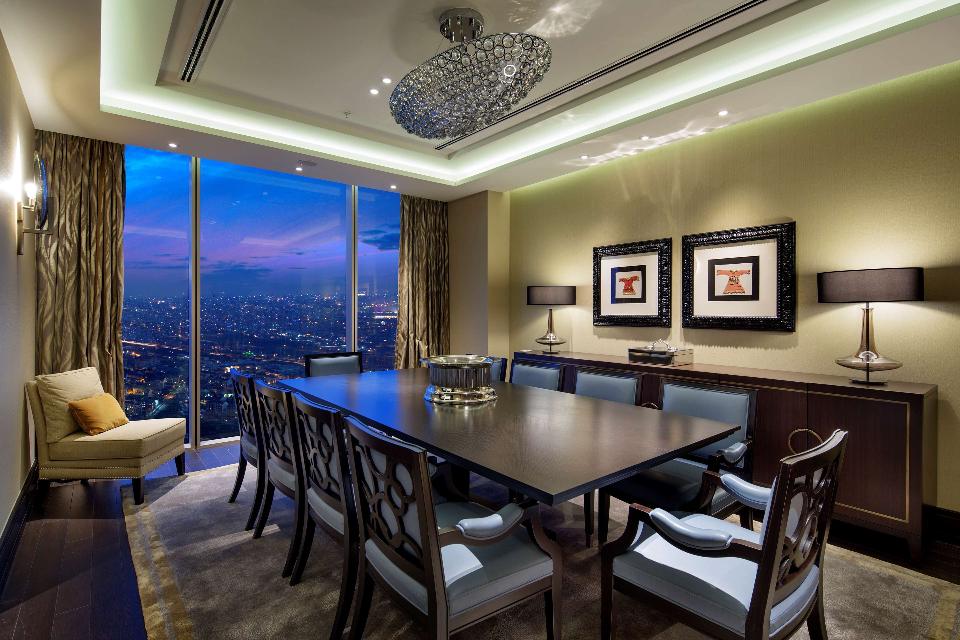 A modern conference room with a large table, chairs, a chandelier, and framed pictures on the wall.
