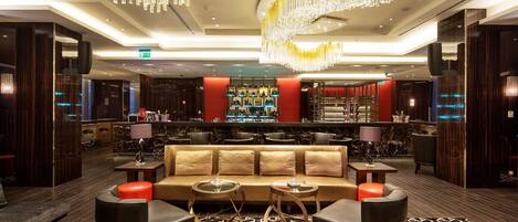 A modern lobby with a central seating area, a bar with a red accent wall, and a patterned carpet.