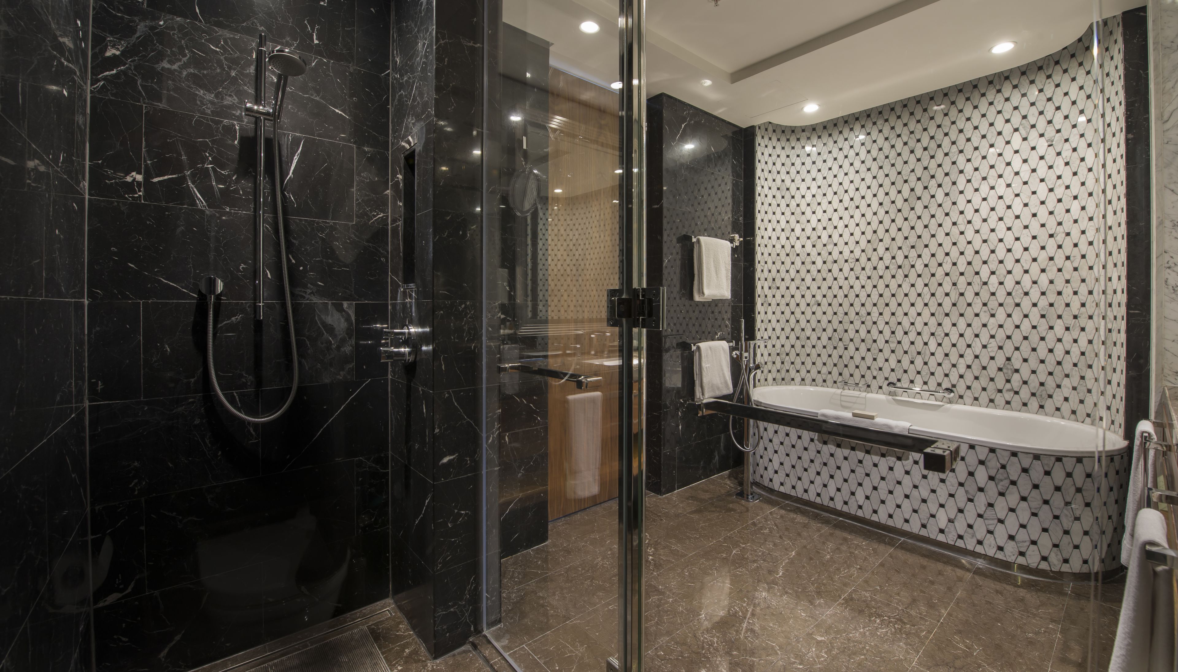 A modern bathroom with a glass-enclosed shower, a freestanding bathtub, and a tiled wall with a geometric pattern.