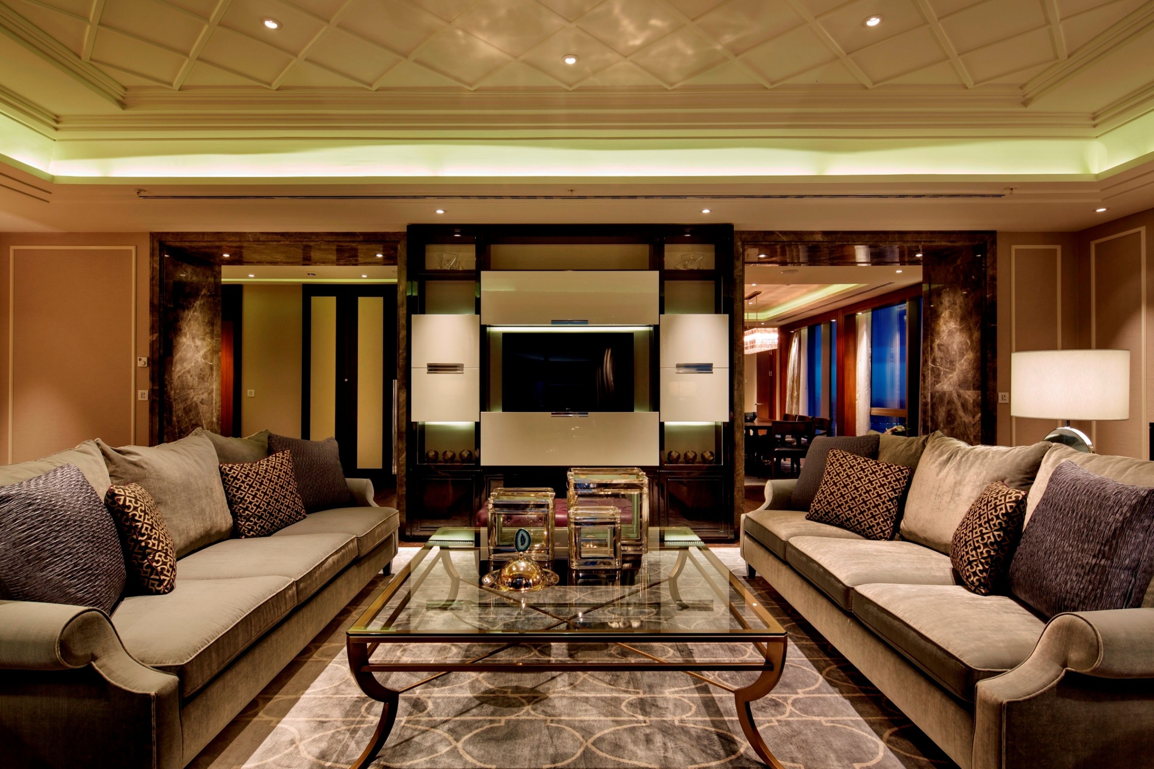 A spacious living room with two sofas facing a central coffee table, a flat-screen TV, and a decorative glass partition.
