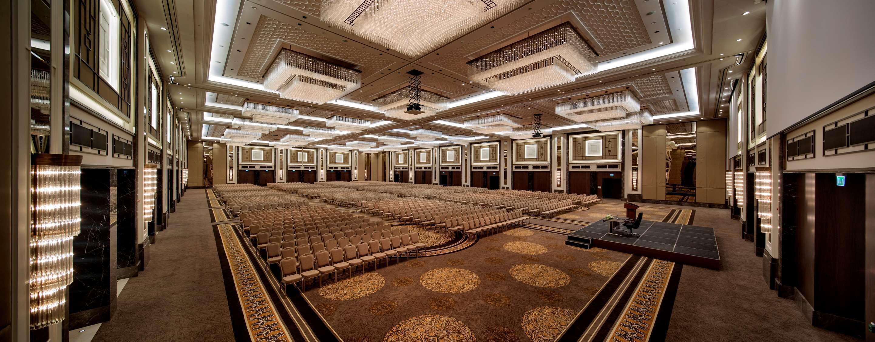 A large, well-lit conference room with rows of chairs, a stage, and a patterned carpet.
