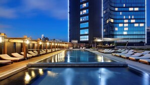 A rooftop pool with sun loungers and a view of a modern building.