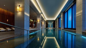 A modern indoor swimming pool with a glass barrier, lounge chairs, and ambient lighting. - Hilton Istanbul Bomonti Hotel & Conference Center (Istanbul)