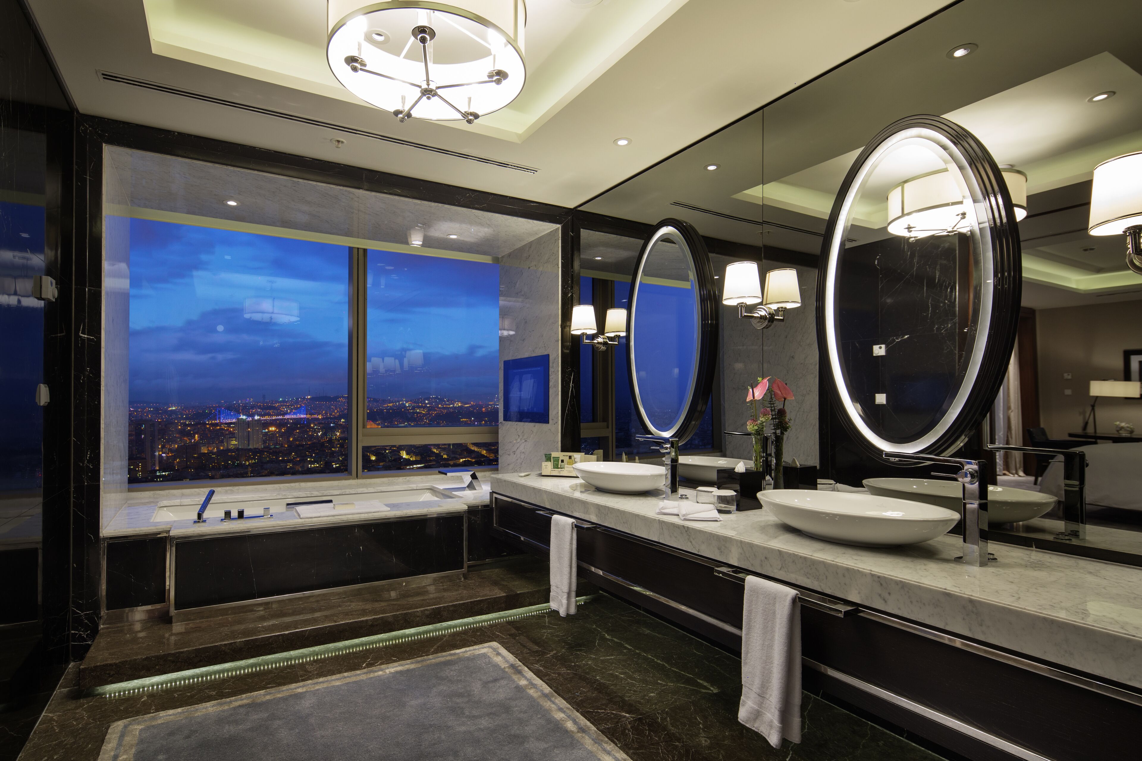 A modern bathroom with a large window, two sinks, and a mirror.