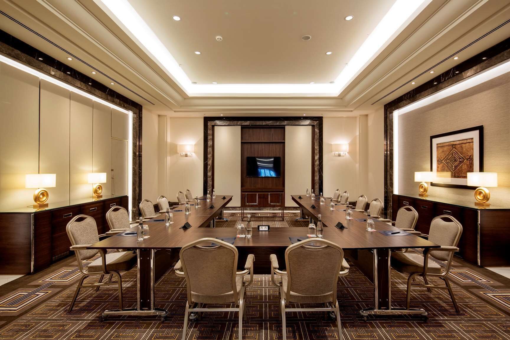 A conference room with a long table, chairs, and a television screen.