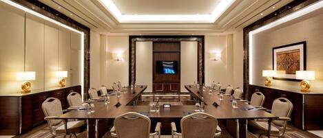 A conference room with a long table, chairs, and a television screen.