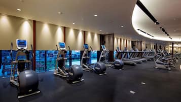 A gym with treadmills, elliptical machines, and stationary bikes arranged in rows.