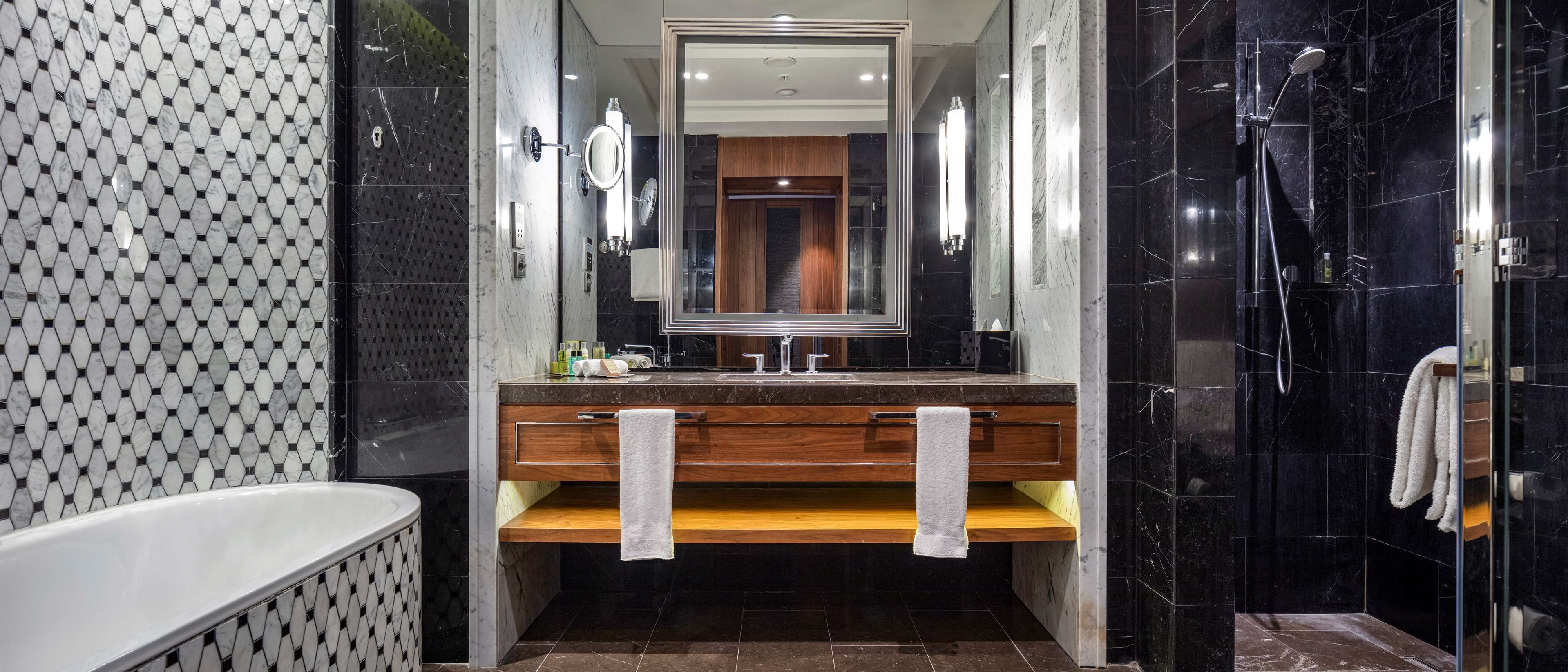 A modern bathroom with a large mirror, a wooden vanity, a bathtub, and a glass-enclosed shower area.