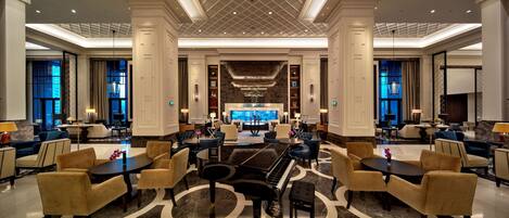 A spacious lobby with a grand piano, comfortable seating, and a large TV screen.