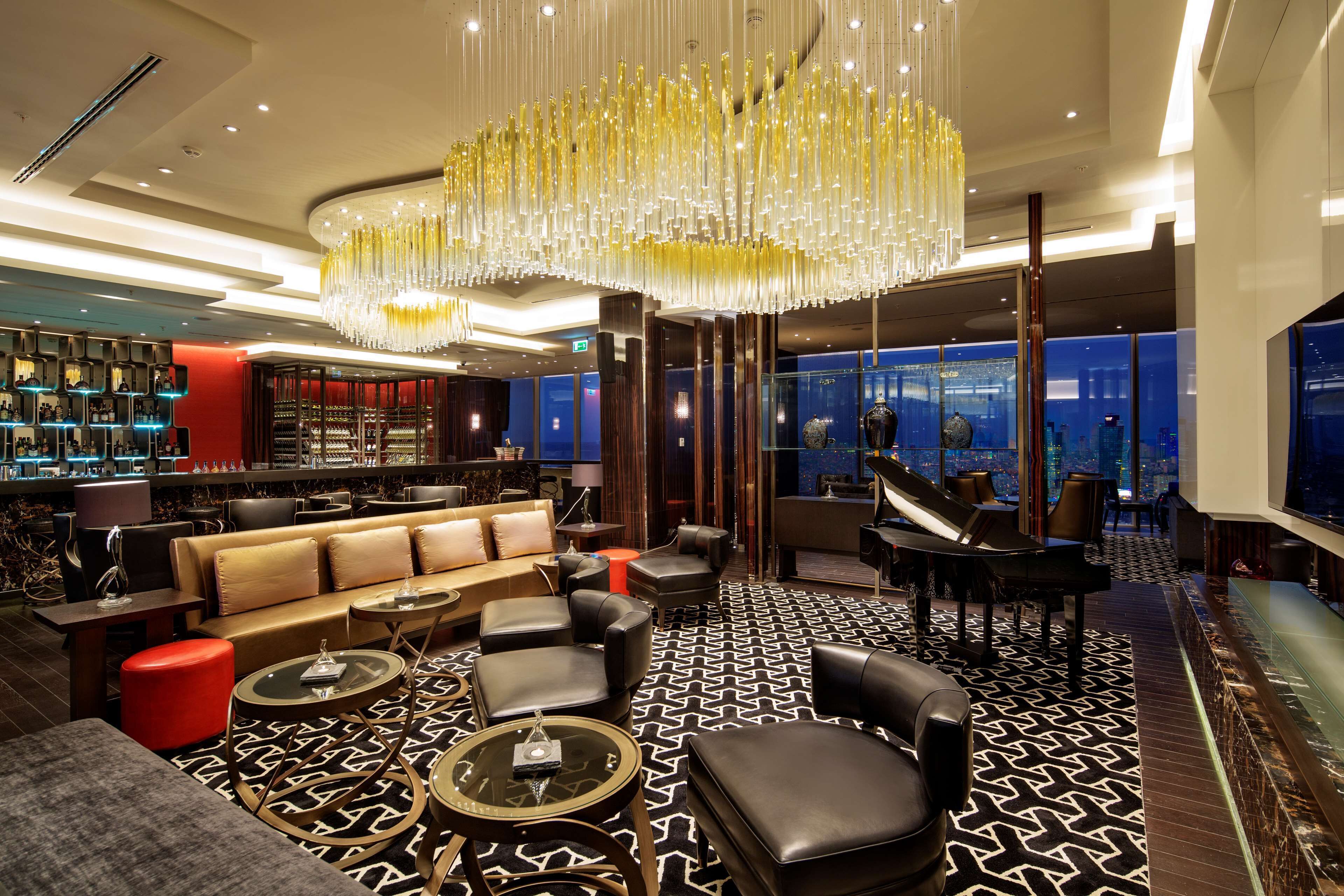 Eine luxuriöse Hotelhalle mit einem prächtigen Kronleuchter, einem Klavier, Ledersitzmöbeln und einer Bar.