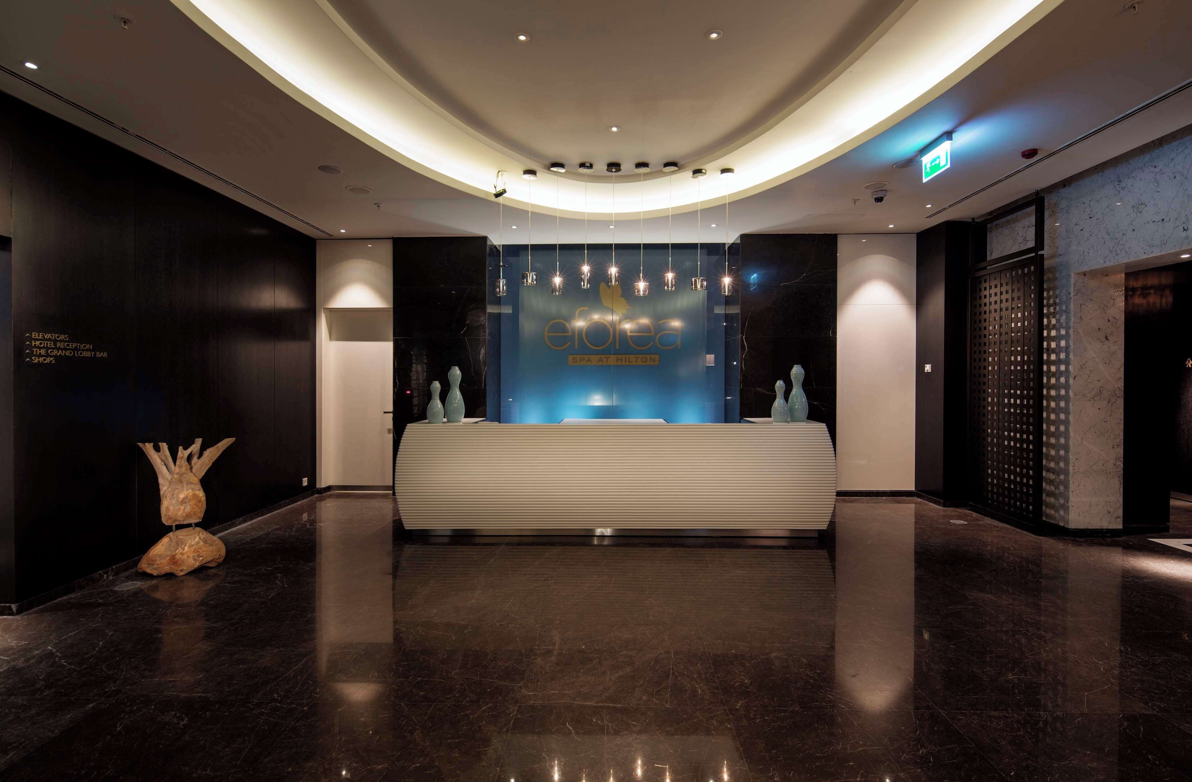 A modern reception area with a marble floor, a reception desk, and a blue wall with the hotel name.