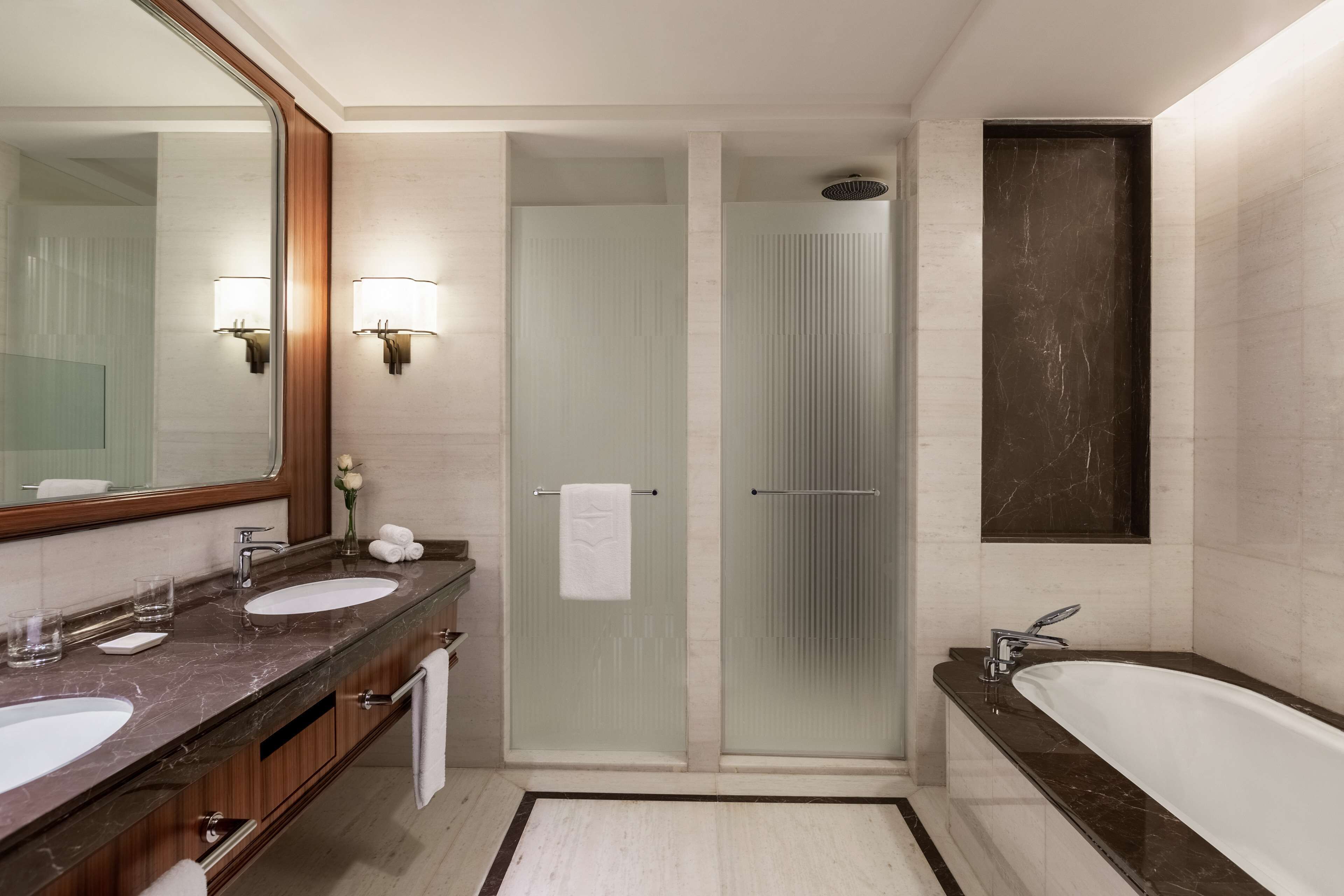 A modern bathroom with two sinks, a large mirror, a bathtub, and a glass-enclosed shower.