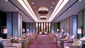A hotel lobby with a long reception desk, multiple seating areas, and a patterned carpet.