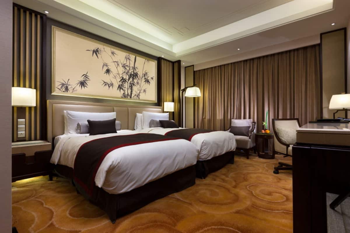 Une chambre d’hôtel avec deux lits, un bureau, une chaise et un grand tableau au mur.