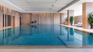 A modern indoor swimming pool with clear blue water, wooden panel walls, and lounge chairs by the pool. - Shangri-La Qufu (Jining)