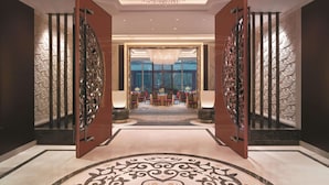 A luxurious hotel lobby with a grand chandelier, ornate wall panels, and a traditional dining area visible through an open doorway. - Shangri-La Qufu (Jining)