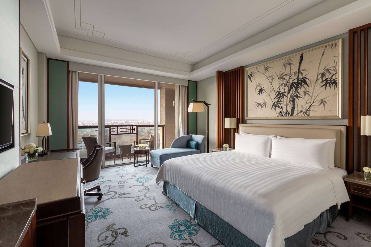 Une chambre d’hôtel avec un grand lit, un bureau, une chaise, un balcon avec vue et un tableau au mur.