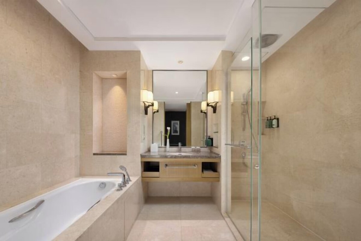 A modern bathroom with a freestanding bathtub, a glass-enclosed shower, and a vanity with a mirror and two wall-mounted lights.