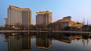 A high-rise hotel with a traditional architectural style, reflecting in a calm body of water. - Shangri-La Qufu (Jining)