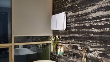 A modern bathroom with a freestanding bathtub, a glass shower enclosure, and a marble wall.