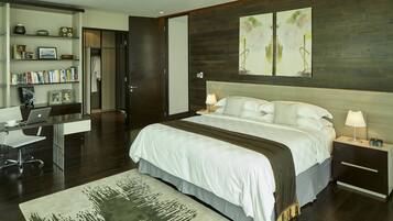 A modern hotel room with a large bed, a desk with a laptop, a bookshelf, and a painting on the wall.