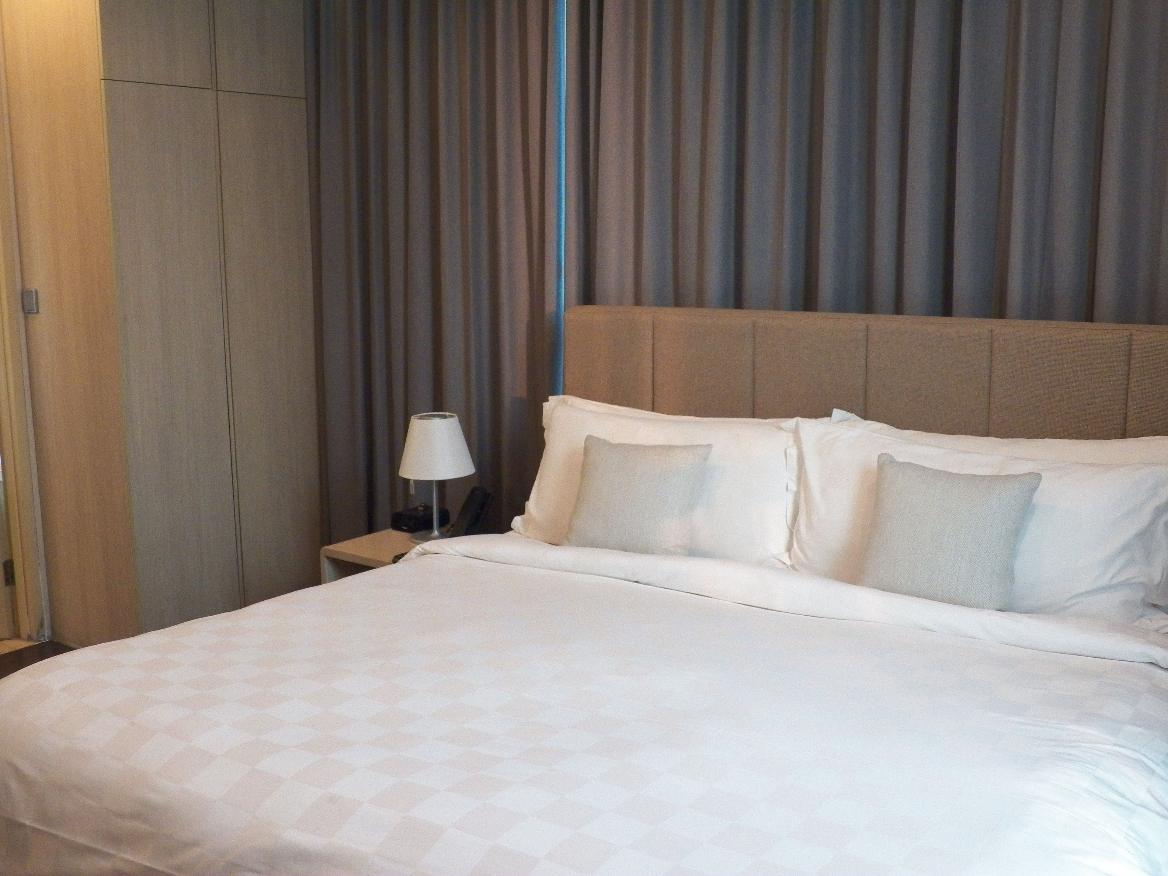 A hotel room with a large bed, a nightstand with a lamp, and a curtain backdrop.
