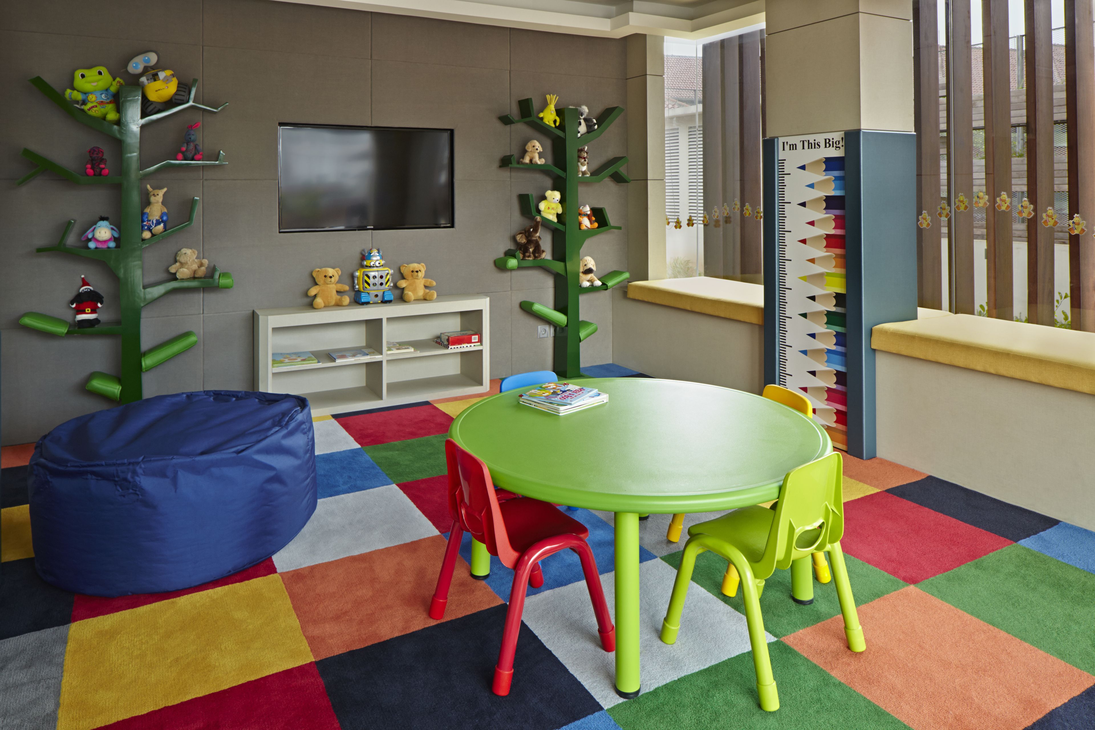 A children's playroom with a green table, colorful chairs, and a bean bag.