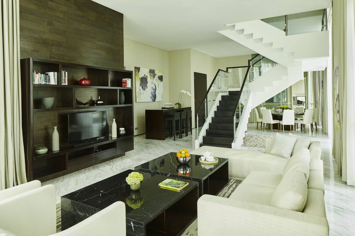 Uma sala de estar moderna com uma mesa de centro preta, sofá branco e uma escadaria que leva a um andar superior.