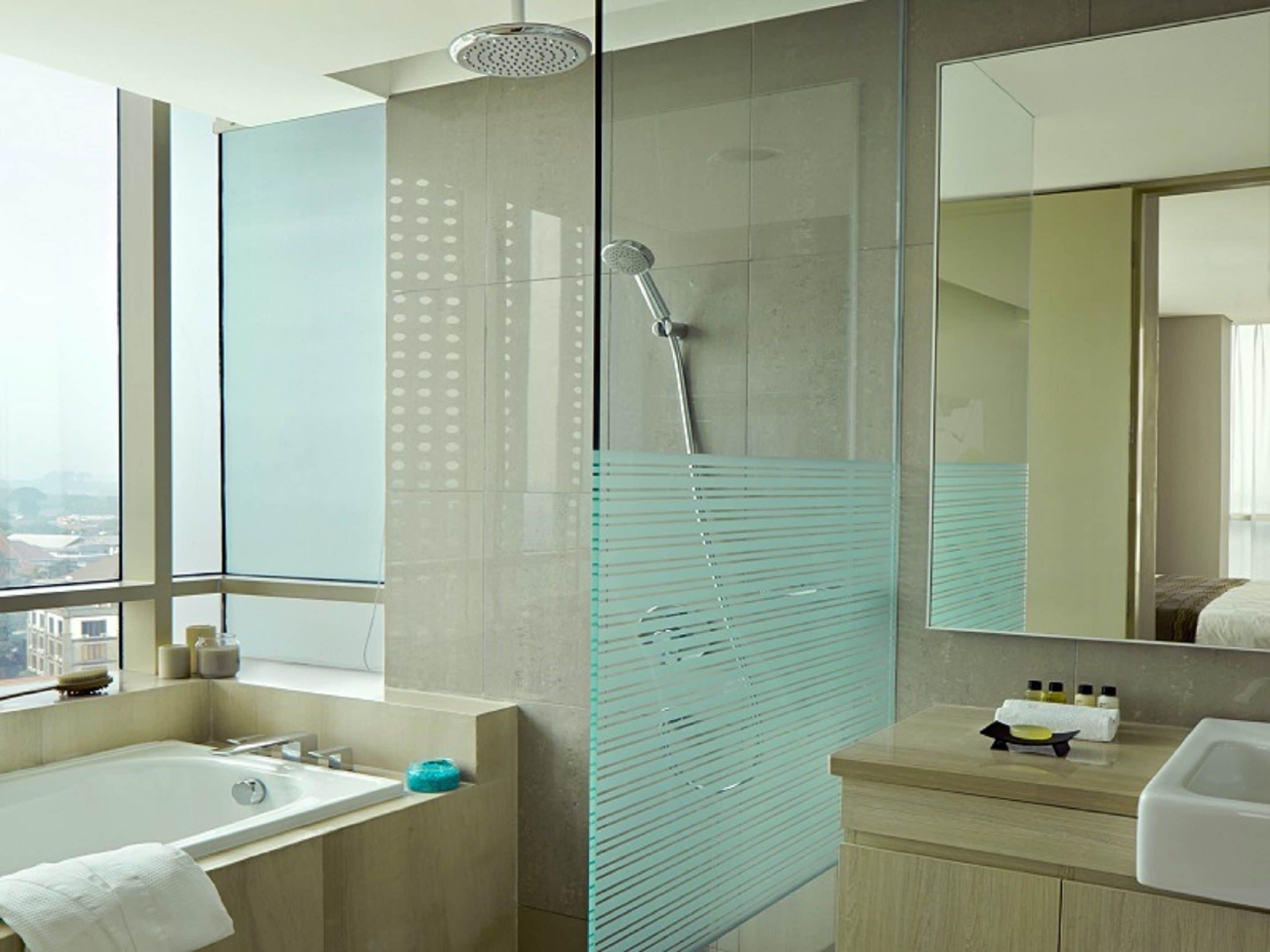 A modern bathroom with a glass shower enclosure, a large mirror, a bathtub, and a vanity with toiletries.