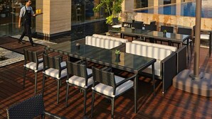 An outdoor patio with tables and chairs, a waiter walking by, and a large glass building in the background. - Fraser Residence Menteng Jakarta (Jakarta)