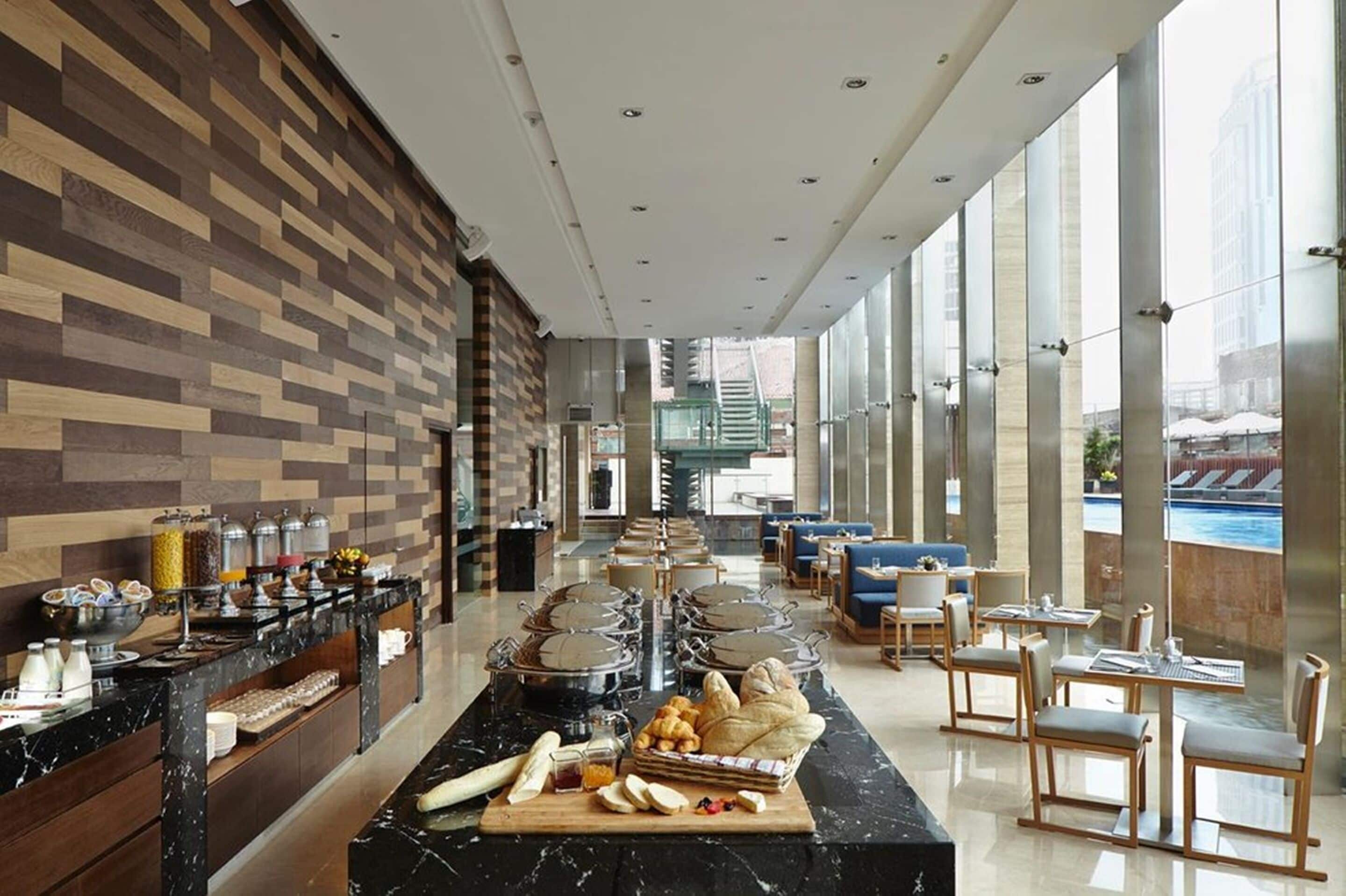 Et hotel lobby med et buffetområde, siddepladser og store vinduer med udsigt til det fri.