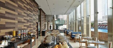 A hotel lobby with a buffet area, seating, and large windows offering a view of the outdoors.