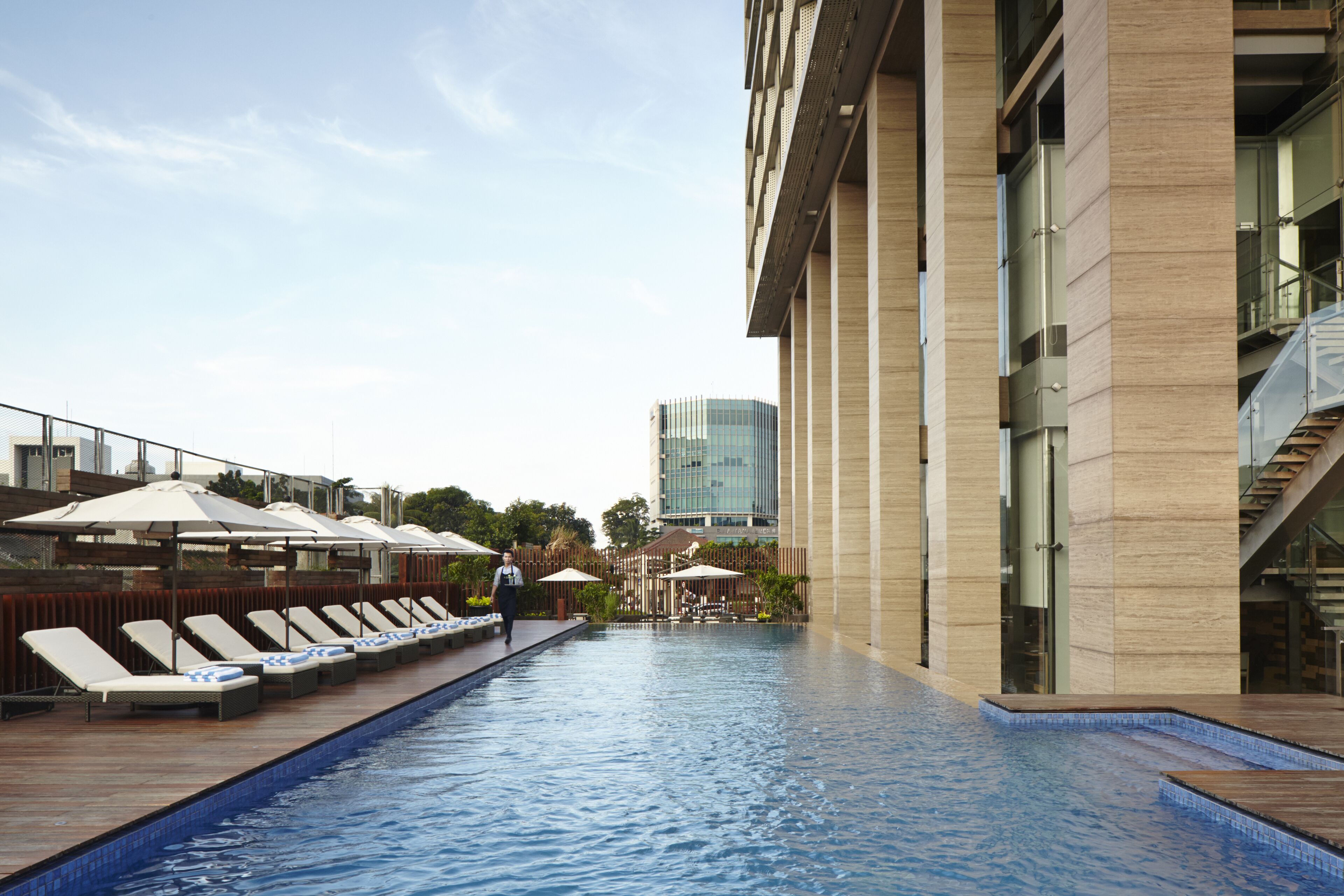 A swimming pool with lounge chairs and umbrellas, a modern building with a glass facade, and a staircase leading to an upper level.
