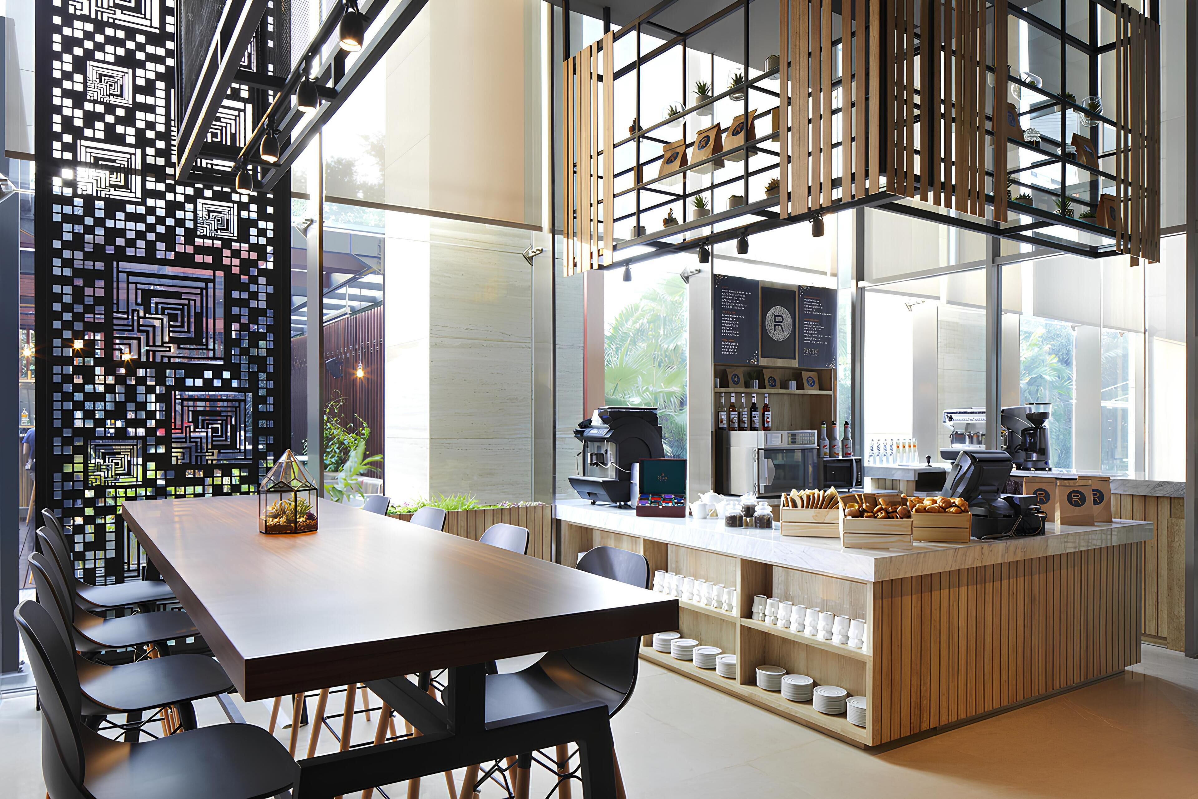 A modern cafe with a wooden table and chairs, a coffee bar with various coffee-making equipment, and a decorative wall with geometric patterns.
