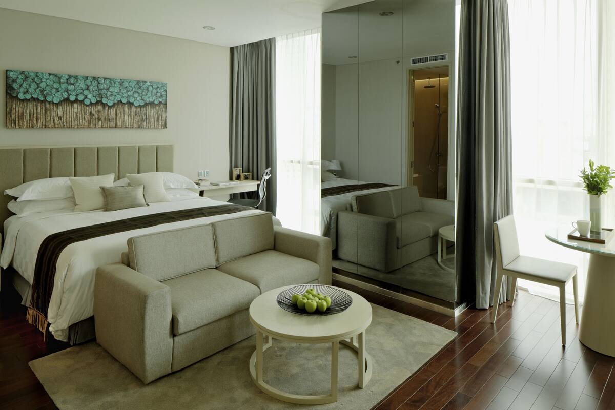Quarto de hotel moderno com cama, sofá, mesa redonda e um espelho grande.