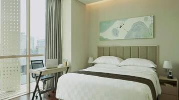 Habitación de hotel con una cama grande, un escritorio con una computadora portátil, una silla y una ventana con cortinas.