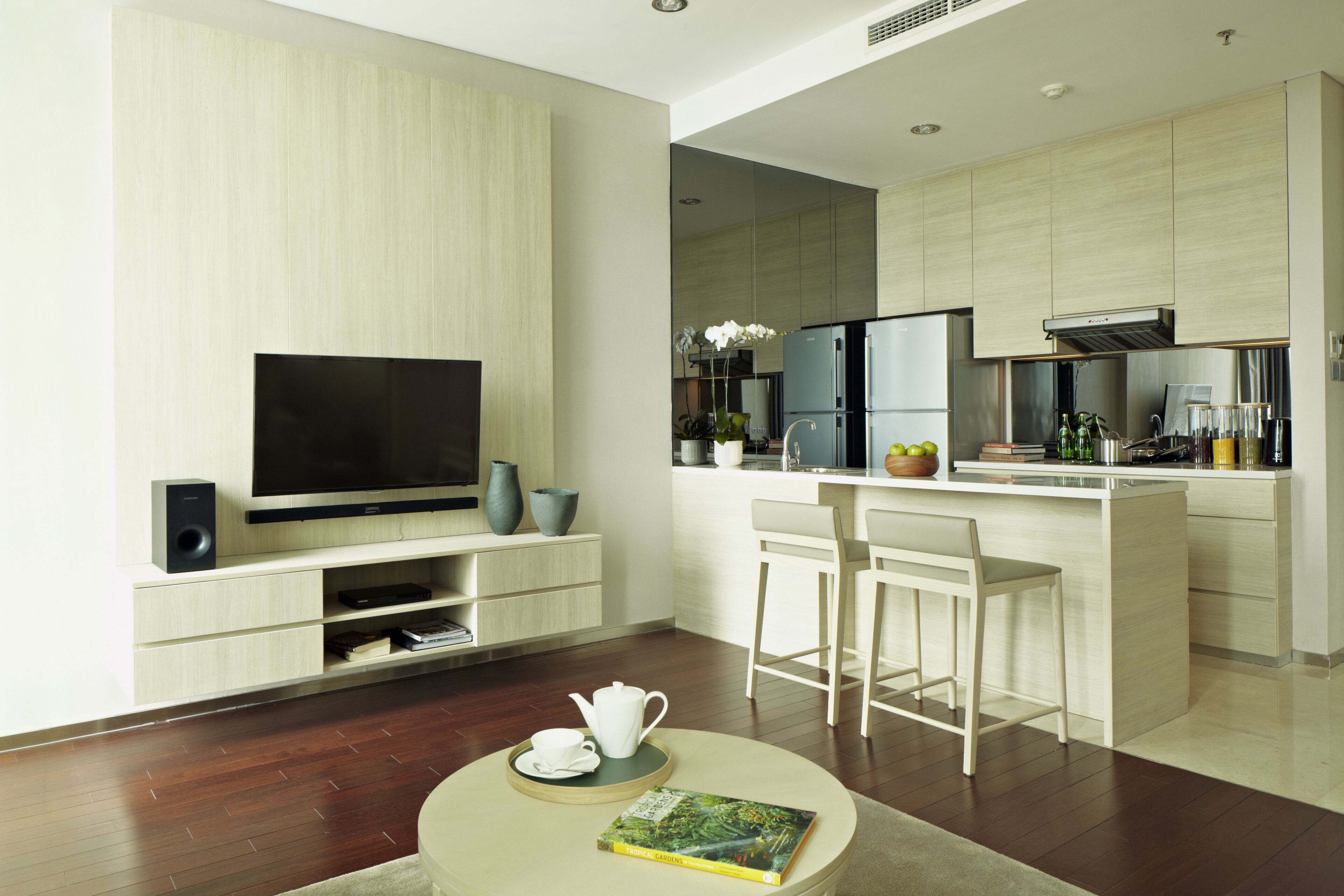 A modern kitchen with a flat-screen TV, a dining area with bar stools, and a small round table with a book and teapot.